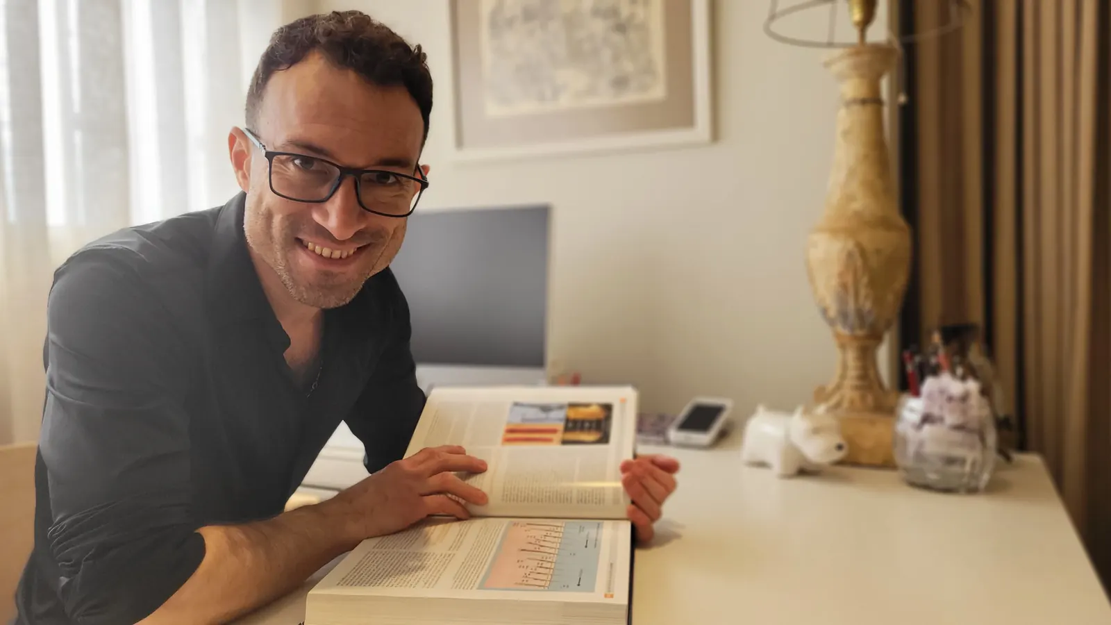 Ricardo Buriticá sonriendo en el escritorio de su estudio de peluquería en Barcelona, con un libro abierto