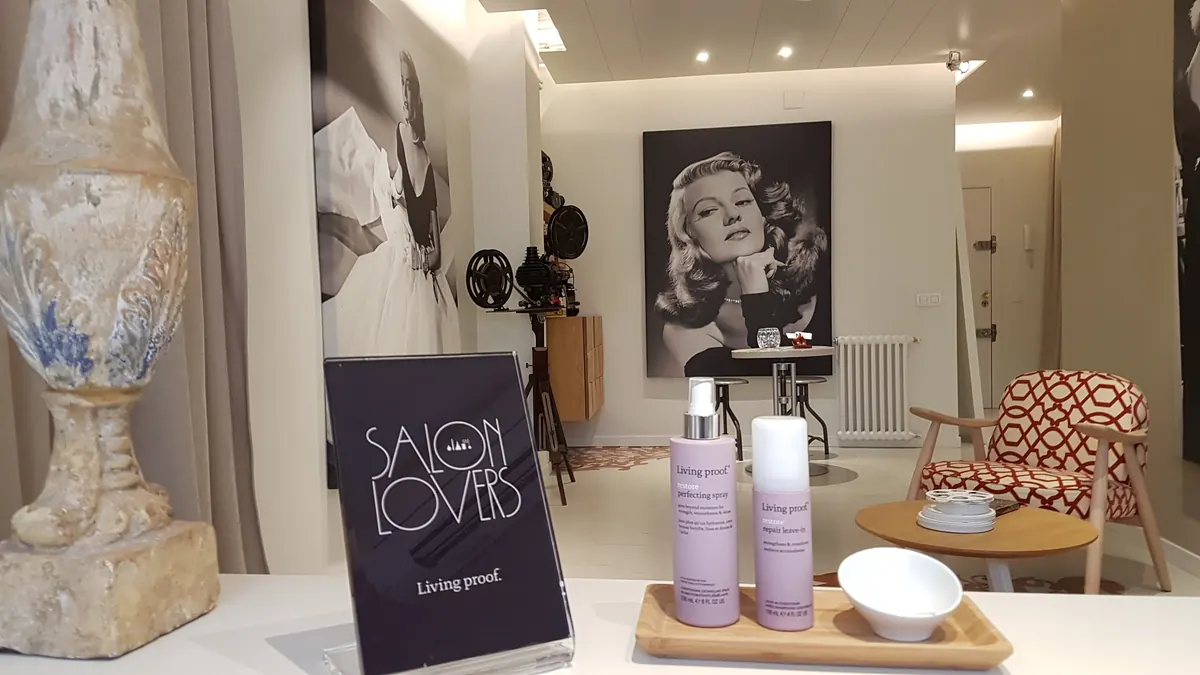 Productos Living Proof y cartel Salon Lovers en el estudio; al fondo, retrato de Rita Hayworth